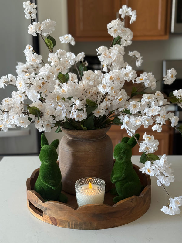 Soft spring moments, simply styled.Fresh white blossoms bring light and movement, while the rich wood vase grounds the look with warmth and texture. Paired with sweet moss bunnies and a soft candle glow, this little arrangement feels like the perfect welcome to the season.It’s the kind of piece that makes a kitchen island, dining table, or coffee table feel instantly refreshed — simple, cozy, and beautifully styled.Sometimes all it takes is a few stems and a warm candle to make a space feel like home. 🌿✨